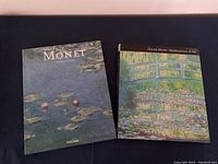 Two books about Monet's paintings laid flat side by side showing their front covers. The left book is published by Taschen and has the title Monet with a cover image of water lilies. The right book is Claude Monet: Masterpieces of Art featuring the Japanese bridge painting on the cover.