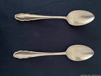 Top view showing two similar silver teaspoons with oval bowls and decorative handles.