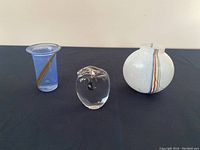 Overview of three blown glass items on black surface: 2 small vases and 1 paperweight