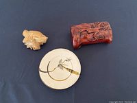 Overview of all three Oriental pieces on dark cloth: carved wooden frog, circular ceramic dish with floral design, and carved wooden box with floral motifs.