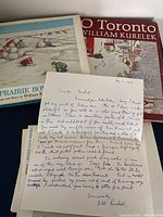 Two hardcover books, one handwritten letter on printed Bill Kurelek letterhead, and two color prints laid flat