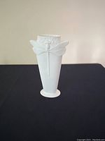White porcelain vase displayed on black surface showing full front including raised dragonfly detail.