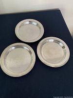 Top view of the three circular silver-plated wine coasters with simple raised rims, showing some surface marks