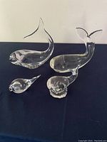 Four clear crystal whale figurines varying in size placed on a dark surface.