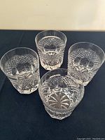 Four crystal whiskey glasses showing diamond and starburst cut patterns, arranged on dark surface.