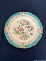 Top-down view of Minton decorative plate showing detailed colorful floral and bird design with turquoise border and gold accents.