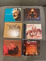 Photo showing 7 CDs with varied French music artists including Felix Leclerc, Edith Piaf soundtrack, Mademoiselle Paris, Paris Je T'aime, and Juliette Greco.
