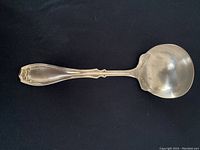 Full view of the silver gravy ladle on a black background showing the detailed handle and ladle bowl.