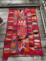 Full view of small handwoven embroidered oriental rug with colorful geometric and abstract patterns, with visible worn fringe.