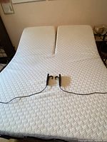 View of queen adjustable bed surface with split head positions and two hand-held remote controls on mattress