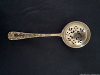 Photo showing the full silver berry spoon with ornate floral and scroll design handle and pierced bowl featuring flower cutouts.