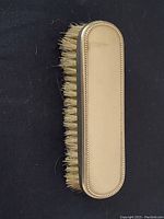 Top view of an antique silver clothes brush with a polished back and beaded edge, natural bristles visible.
