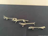 Photo showing four silverplate animal-shaped cutlery rests including a frog, dog, bird, and fish, arranged in a row on a dark surface.