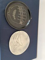 Two Indigenous decorative plates, one black ceramic with etched design, one pewter with embossed design.