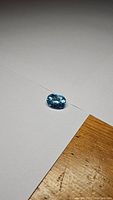 Close-up photo of oval cut Swiss blue topaz gemstone on white paper, showing top and side facets.