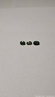 Three small oval cut green sapphires side by side on a plain background, showing size and color