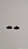 Two deep hot pink purple trillion cut sapphires displayed side-by-side on a light surface.