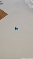 Photo showing deep blue princess cut London Blue Topaz gemstone on a white background with strong sparkle and reflections.