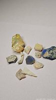 Wide shot of 11 rough opal pieces of various sizes showing color flashes including green, blue, yellow, and purple.