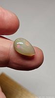 Close-up of pear-shaped natural untreated Ethiopian opal held between fingers showing color flashes.