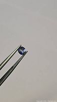 Close-up image of oval cut blue Ceylon sapphire held with tweezers showing color and clarity