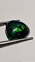 Close-up of jet black Ethiopian opal showing green color flashes with trillion cabochon shape