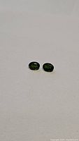 Pair of deep green oval chrome diopside gemstones shown clearly on white background.