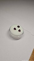 Photo showing three loose rubies in a round clear container with white foam padding, arranged in triangular layout.