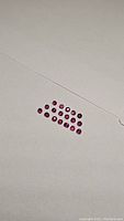 Eighteen calibrated round cut rubies arranged in rows on white background showing consistent size and color.