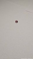 Photo of a small round cut pink-orange Padparadcha sapphire gemstone on a neutral background, showing its color and clarity.