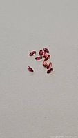 Ten loose natural padparadscha marquise cut sapphires scattered on a neutral flat surface, showing their deep pink to orange hues and faceted surfaces.