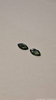 Pair of marquis cut green sapphires placed on a plain surface showing size and color