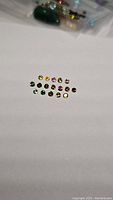 Photo showing 18 small round cut rainbow tourmaline gemstones laid out in rows on white background, showing varied vibrant colors from green, yellow, pink to brown.