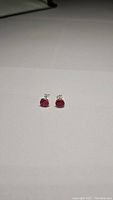 Pair of small round natural ruby stud earrings set in sterling silver on a white background, front view