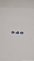 Three pear-shaped natural tanzanite gemstones laid in a row on a beige background, showing their purple blue color and clarity.