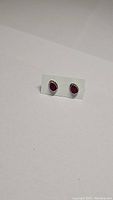 Pair of pear-shaped natural ruby earrings set in 925 sterling silver, shown on card backing against white background, highlighting color and setting.