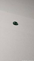Oval cut natural Zambian emerald gemstone with visible inclusions on a plain light surface.