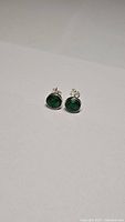 Pair of stud earrings with round green emerald gemstones set in sterling silver, shown from front angle.