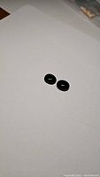 Two oval cabochon jet black onyx gemstones placed on white background showing smooth glossy surface and intense black color.