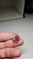Ring held between fingers showing top and side angles highlighting large orange sapphire and surrounding colored stones.