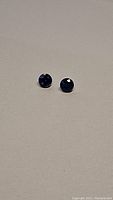 Two round-cut royal blue kyanite gemstones placed on a light-colored surface, showing their size and color.