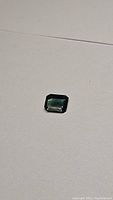 Octagon cut blue green sapphire gemstone lying on plain surface showing deep color and cut shape.