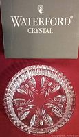Photo showing clear crystal bottle coaster with intricate cut pattern and original Waterford Crystal box in background