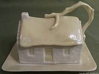 Front view of the covered butter or cheese dish shaped like a cottage with a handle that looks like a tree branch, sitting on the base plate.