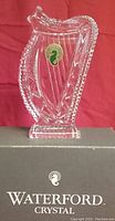 Clear Waterford Irish Crystal harp-shaped paperweight with Waterford sticker on front standing on the box that has Waterford logo and text.