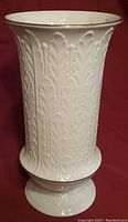 White porcelain vase with embossed leaf designs and gold trim at rim and base, photographed against a red background.