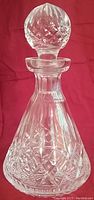 Full view of clear Lismore pattern Waterford crystal decanter with stopper against red background.