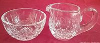 Photo showing the Waterford Irish Crystal Lismore pattern small sugar bowl and creamer on a red surface.