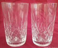 Pair of clear Waterford Irish Crystal tumbler glasses in Lismore pattern with detailed diamond cuts, standing side by side against a red background.