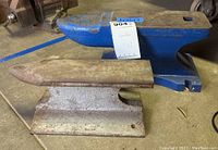 Pair of anvils side by side showing size comparison, larger blue painted Central Forge anvil with label and smaller unmarked, rusted cast iron anvil.